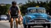 Un ciclista con máscara como medida de precaución contra la propagación del coronavirus lleva un pollo en la mano mientras pedalea su bicicleta en La Habana. (AP Foto/Ramón Espinosa)