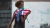 Una mujer con una máscara protectora contra el coronavirus y una bandera de EEUU camina por una calle de La Habana. (Yamil Lage/AFP)